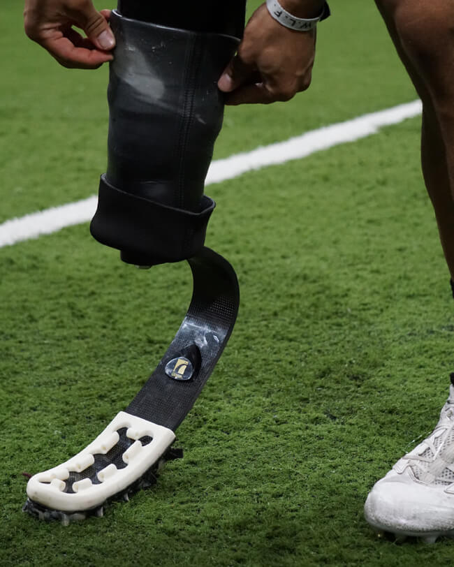 Close up of person adjusting sock on prosthetic cleat while standing on a football field